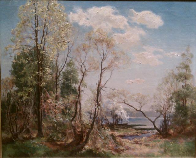 A few bare trees, a few with leaves against a blue sky with white clouds.