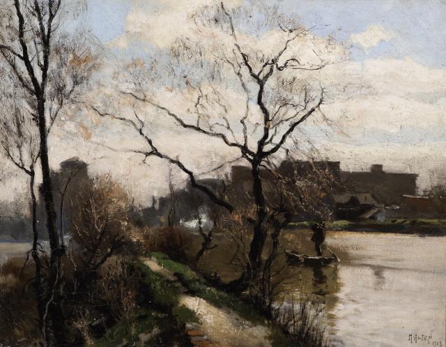 Leafless trees on a small hill near a river with buildings in the background.