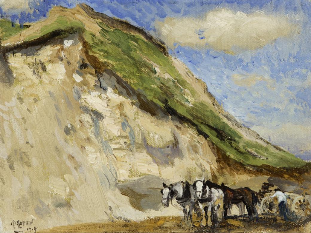 Horses near a large sand dune with green grass on top.