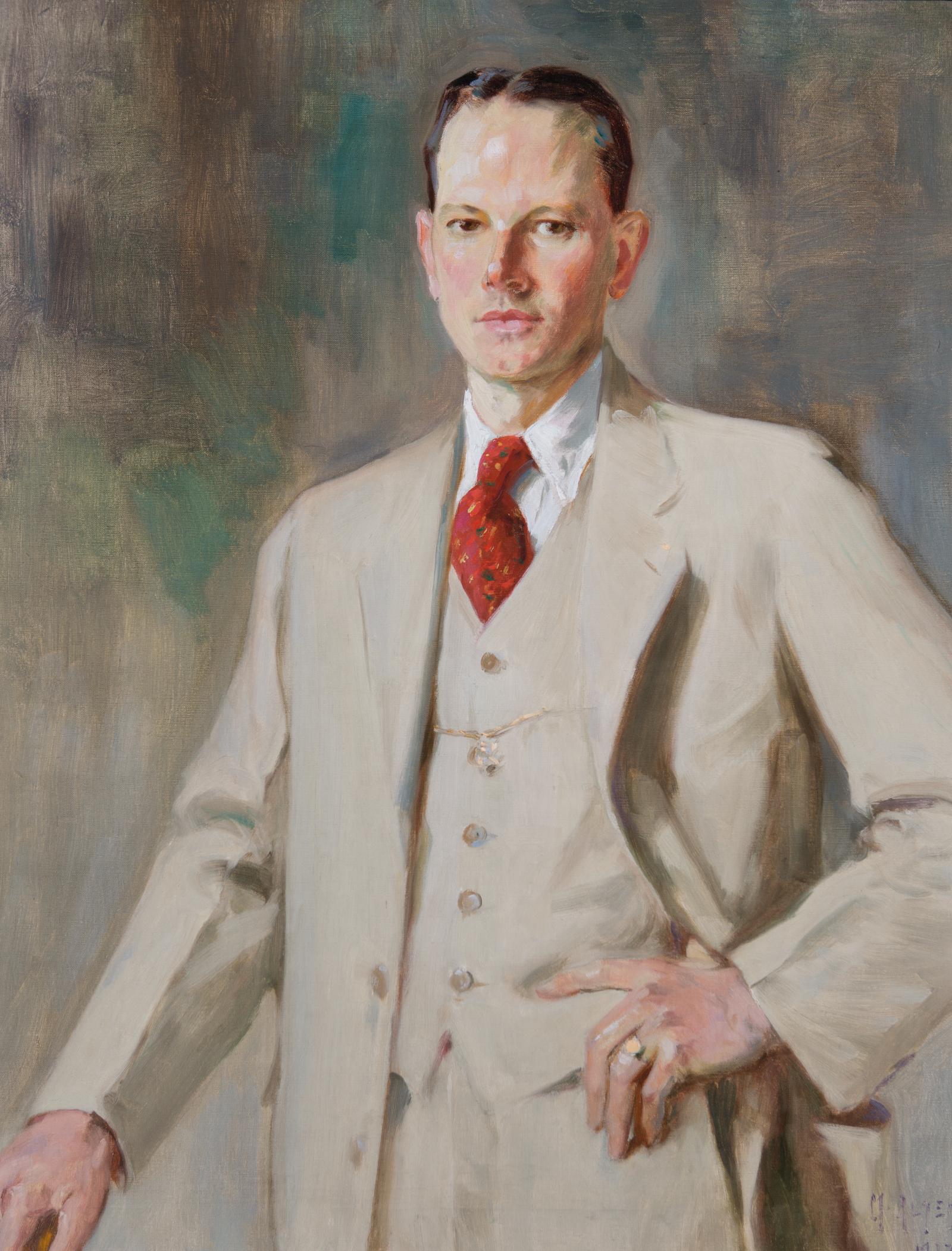 Portrait of man standing with one hand on left hip; wearing light-colored suit with red tie tucked into it.