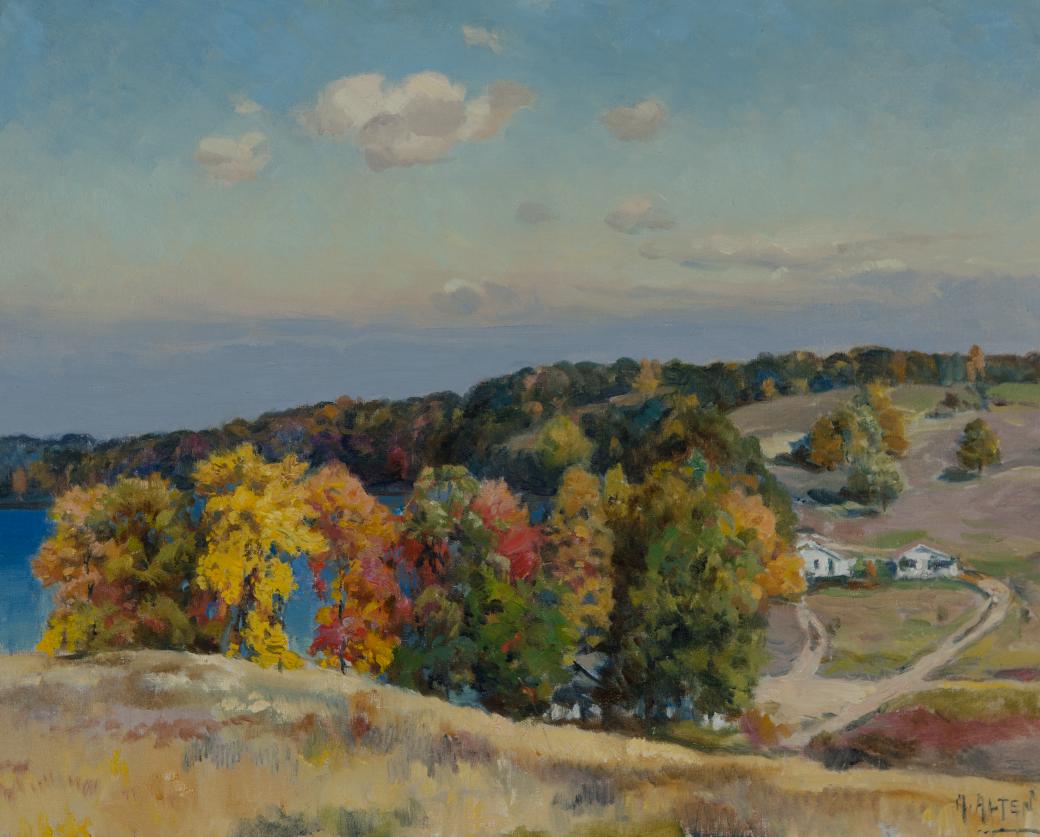 Water on view from a hill, multi-colored trees and buildings below the hill.