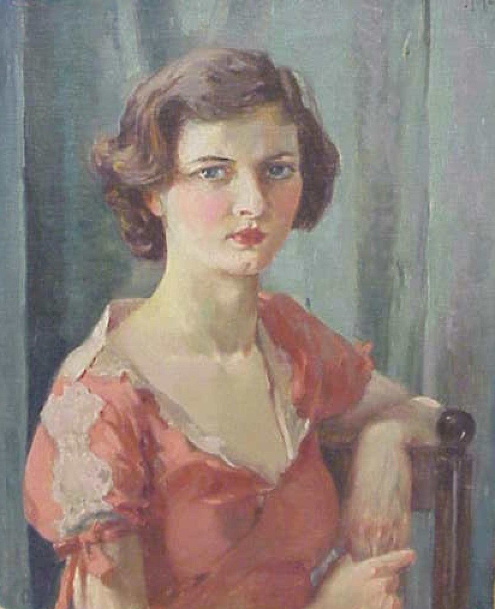 Young woman in pink dress seated in wooden chair with one elbow resting on the back of the chair.