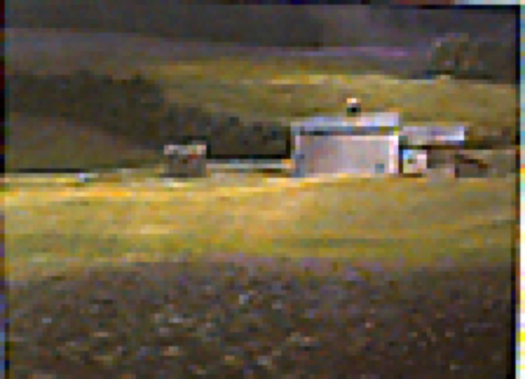 Landscape featuring cluster of barns with yellow fields and lavender foliage; green in front; with stormy dark sky.