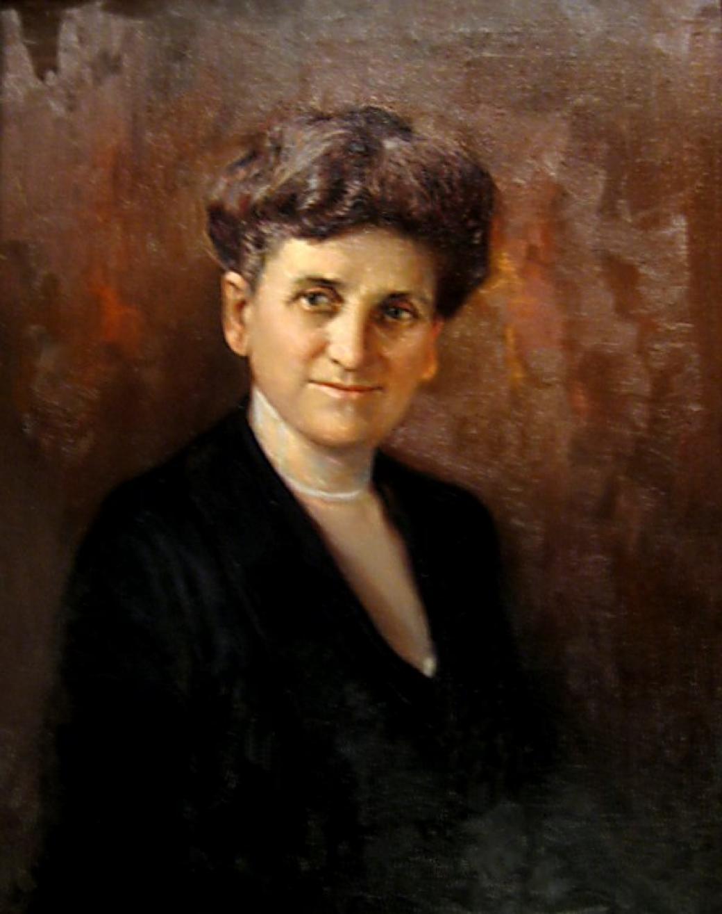 A portrait of an aging woman in a sophisticated black dress wearing a white necklace with her hair piled atop her head, pinned up.