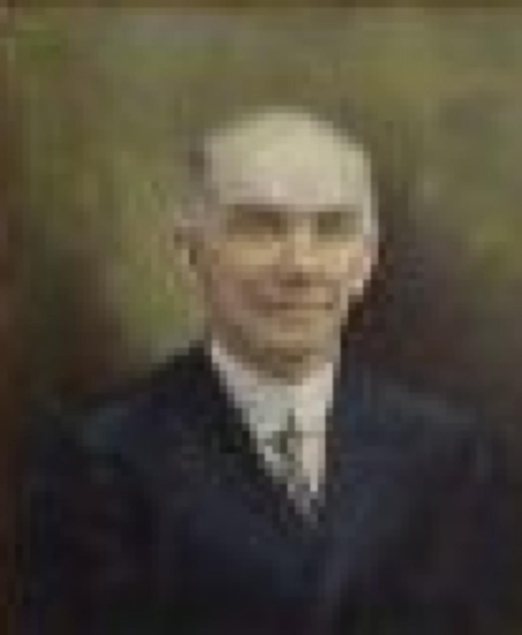 Protrait of man in black suit with blue and yellow tie on green background.