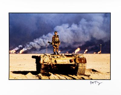 An American soldier stands on top of a destroyed Iraqi tank. Kuwaiti oil wells, ignited by Saddam's retreating forces, burn in the distance, Kuwait