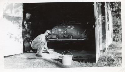 Untitled (Man in Baseball Cap Crouches in Front of a Car)